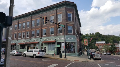 Historic brick building with shops on the ground floor, located at a street intersection under a partly cloudy sky.