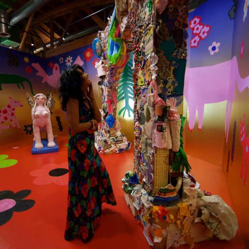 A person in a floral dress admires a colorful art installation surrounded by vibrant murals and sculptures.
