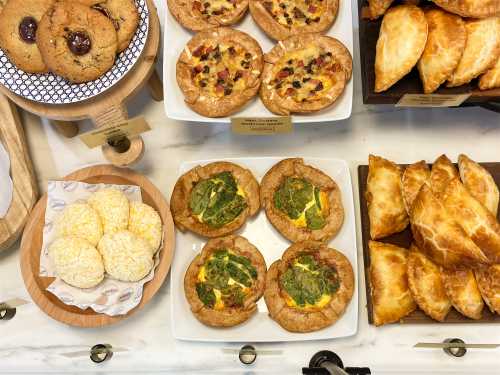 A display of baked goods including cookies, savory pastries, and quiches with spinach on a marble countertop.