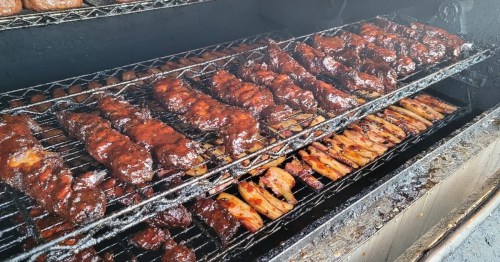 A close-up of a smoker filled with various meats, glistening with barbecue sauce, cooking on metal racks.