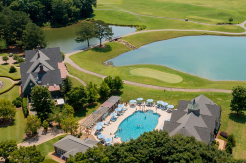 Aerial view of a resort with a pool, lounge chairs, and a golf course surrounded by greenery and a pond.