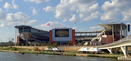 Baylor University stadium with "Baylor Bears" sign, surrounded by clouds and a river, viewed from a nearby bridge.