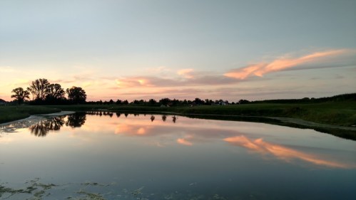A serene landscape featuring a calm river reflecting a colorful sunset with trees and fields in the background.