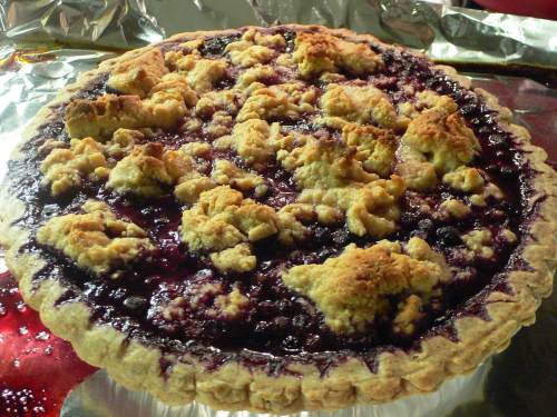 A freshly baked berry pie with a crumbly topping, resting on a shiny surface.