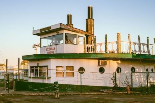 A vintage boat converted into an ice cream shop, featuring a deck and two smokestacks, set against a clear sky.