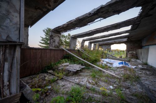 An abandoned building with crumbling walls, overgrown vegetation, and debris scattered on the ground.