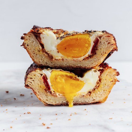 A close-up of two halves of a baked bread dish with a runny egg yolk and crispy edges, resting on a marble surface.