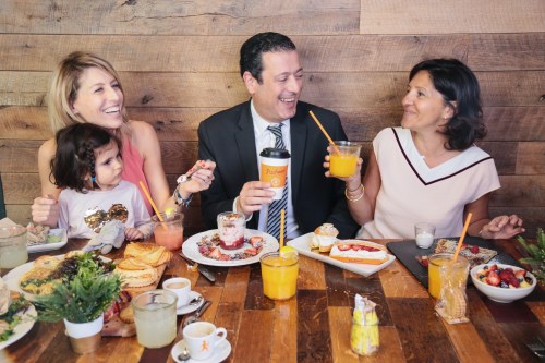 A group of four people enjoying a lively breakfast with various dishes and drinks on a wooden table.