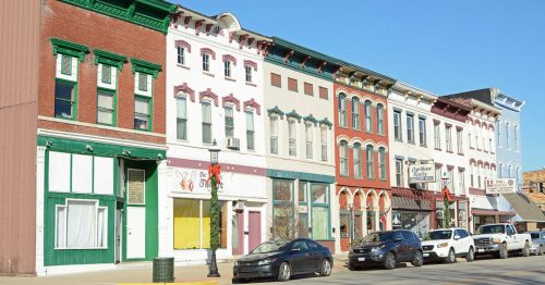 Colorful historic buildings line a street, showcasing a mix of architectural styles and storefronts under a clear blue sky.