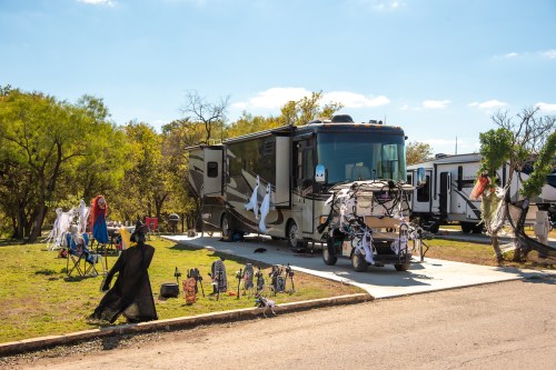 An RV decorated for Halloween with ghostly figures and spooky decorations in a campsite setting.
