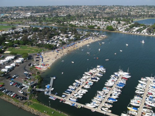Aerial view of a marina with boats, a beach area, and a residential area in the background.