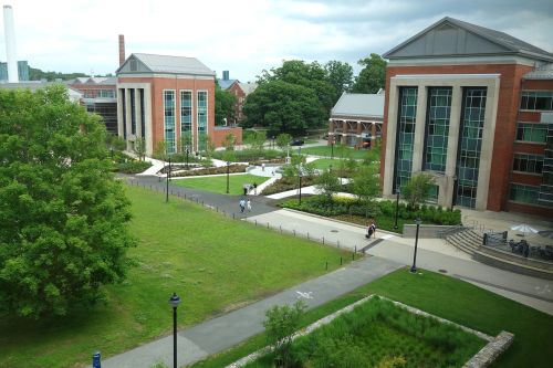 A view of a campus with modern buildings, green lawns, and pathways, under a cloudy sky.