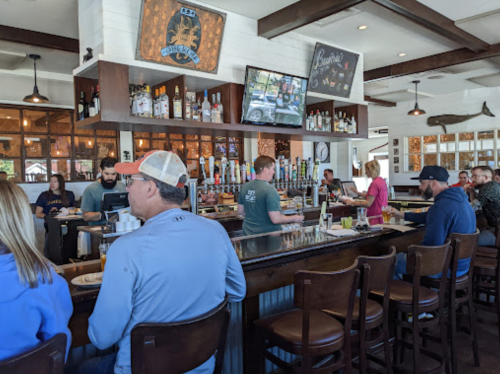 A lively bar scene with patrons seated at the counter, a bartender serving drinks, and a TV displaying a sports event.
