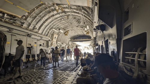 Interior of a large aircraft with people walking and sitting along the sides, showcasing a spacious, industrial design.