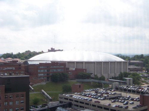 A large, domed sports arena surrounded by buildings and parking lots under a cloudy sky.