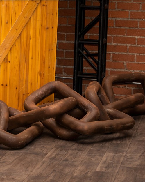 A wooden wall with a diagonal pattern and large, rusted metal chains on a wooden floor.