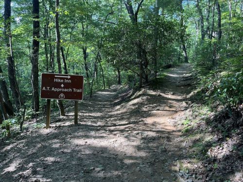 A wooded trail with a sign pointing to "Hike Inn" and "A.T. Approach Trail" amidst lush greenery.