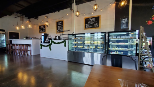 A cozy café interior featuring display cases of desserts, a counter, and bar seating under warm pendant lights.