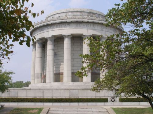 A circular stone monument with columns, surrounded by trees, dedicated to the American Revolution.