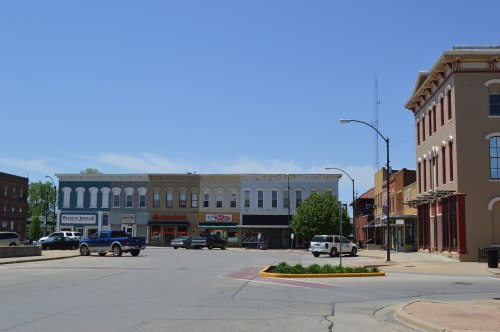 A small town street scene featuring storefronts, parked vehicles, and clear blue skies.