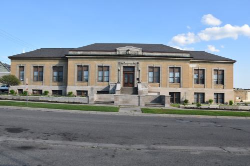 Historic building with a stone facade, large windows, and a central entrance, set against a clear blue sky.