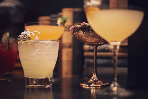 A variety of colorful cocktails on a bar, featuring garnishes and elegant glassware.