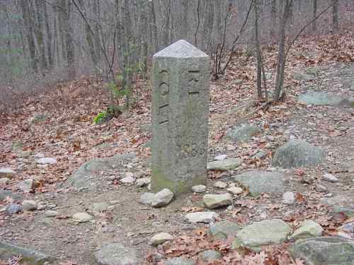 A stone marker with the year 1882, surrounded by rocky terrain and leafless trees in a wooded area.