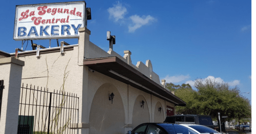 Sign for "La Segunda Central Bakery" on a building with parked cars and a clear blue sky.