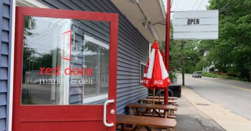 A red door leads to a market and deli, with outdoor seating and an "OPEN" sign visible.