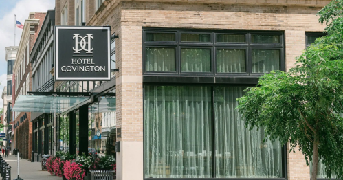 Exterior of Hotel Covington, featuring a sign, large windows, and flower beds along the sidewalk.