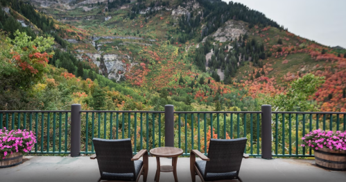 A scenic view of colorful autumn foliage from a balcony with two chairs and a small table.
