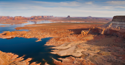 A vast desert landscape with a winding river, rocky formations, and distant mesas under a clear blue sky.