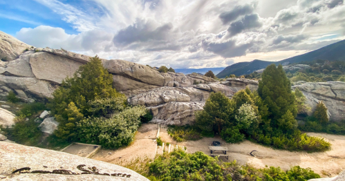 A scenic view of rocky terrain with trees and a cloudy sky in the background.