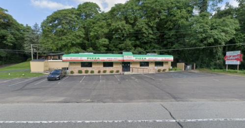 A pizza restaurant with a green and red sign, surrounded by trees, and a mostly empty parking lot.