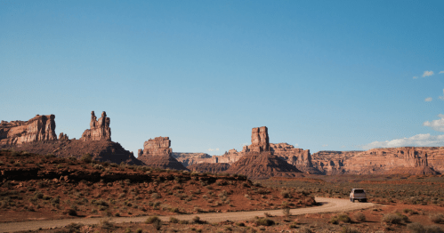 A scenic desert landscape with towering rock formations and a winding dirt road under a clear blue sky.