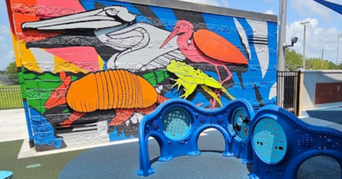 Colorful mural featuring various animals, including a pelican, armadillo, and frog, beside blue playground equipment.