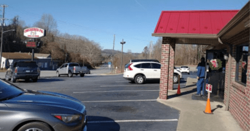 A parking lot with several cars and a brick building with a red roof, near a sign for a restaurant.