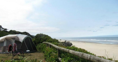 A tent set up near a beach, with a view of the ocean and a cloudy sky in the background.