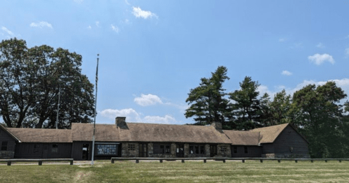A rustic building with a thatched roof, surrounded by trees and a clear blue sky.