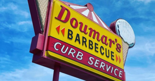 Brightly colored sign for Doumar's Barbecue Curb Service against a blue sky, featuring arrows and a vintage design.