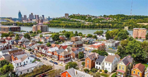 Aerial view of colorful houses with a river and city skyline in the background, surrounded by greenery.