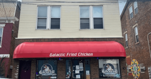 Exterior of a restaurant called "Galactic Fried Chicken" with a red awning and large windows above.