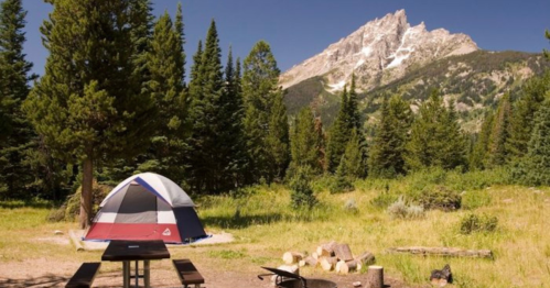 A colorful tent set up in a lush campsite with a mountain backdrop and a picnic table nearby.
