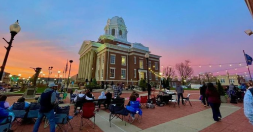 A vibrant sunset over a historic courthouse, with people gathered on the plaza enjoying the evening.
