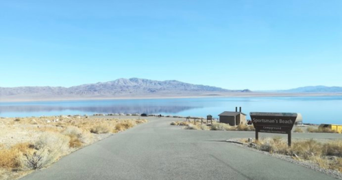 A scenic view of Sportsman's Beach campground, with mountains and a calm lake in the background under a clear blue sky.