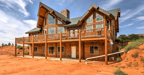A large wooden house with a balcony, set against a backdrop of red sand and blue sky.