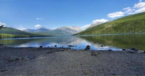 A serene lake surrounded by mountains and lush greenery under a clear blue sky.