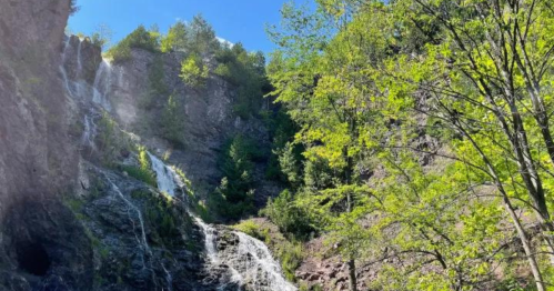 A scenic waterfall cascading down rocky cliffs, surrounded by lush green trees under a clear blue sky.