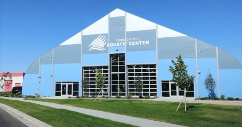 Exterior of the Idaho Central Aquatic Center, featuring a large blue and white building with glass doors and landscaping.