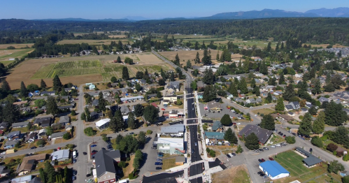 Aerial view of a small town surrounded by fields and mountains, featuring residential areas and a main street.